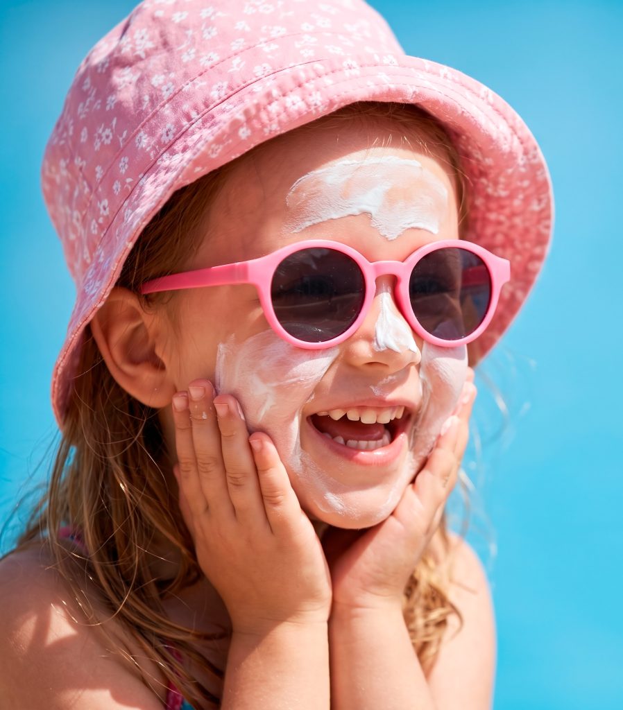 Niña protegiéndose la cara del sol con crema solar
