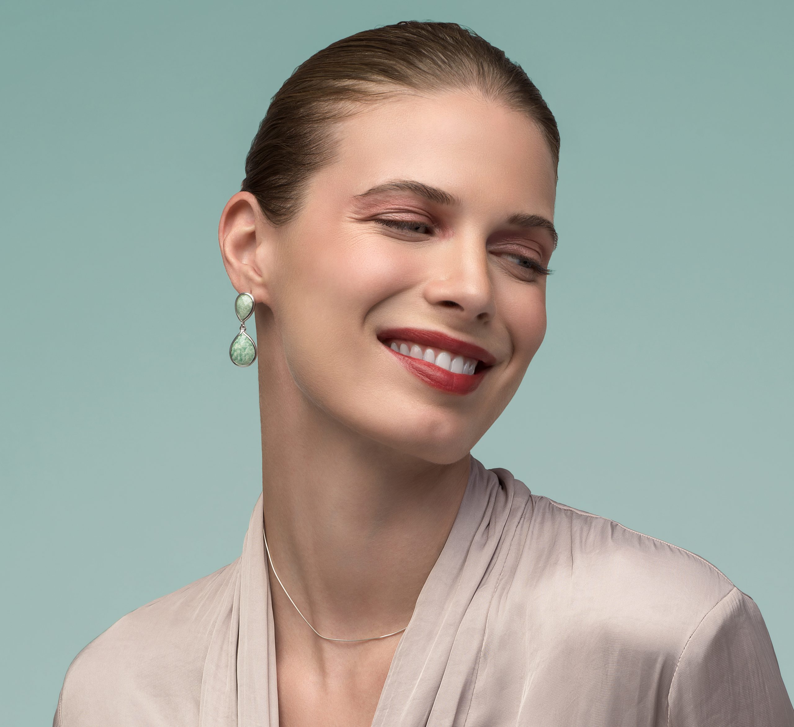 modelo Mujer sonriente luciendo pendientes de amazonita natural en forma de lágrima de Cristian Lay combinados con ropa en tonos neutros.